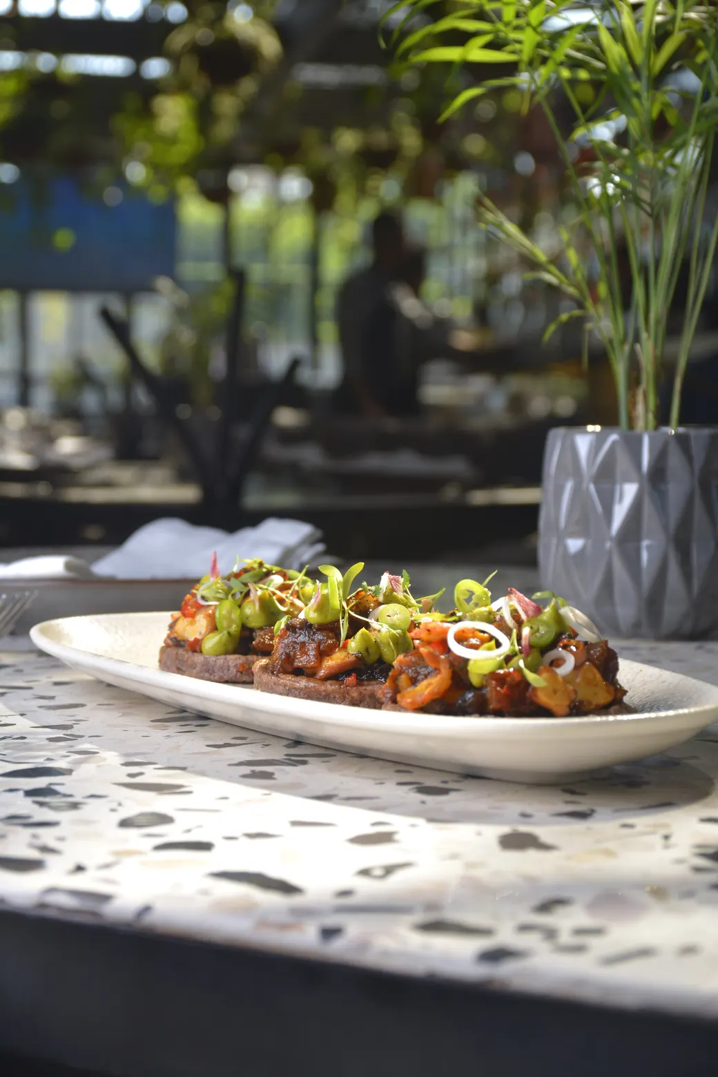 Sopes de pulpo con chicharrón sobre un plato blanco alargado, en la terraza de Brick